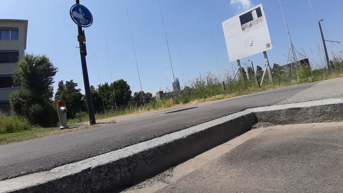 Blick auf einen Randstein, dahinter ein ausgestecktes Bauprojekt. 